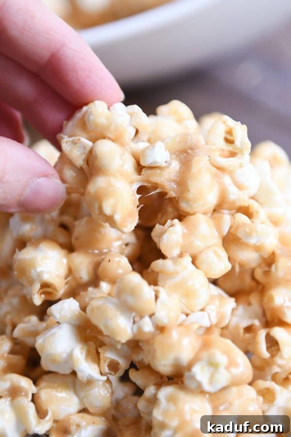 Gooey Peanut Butter Popcorn Bliss 3 A hand gently pulling a cluster of soft and chewy peanut butter caramel popcorn from a larger batch, highlighting its irresistible texture.