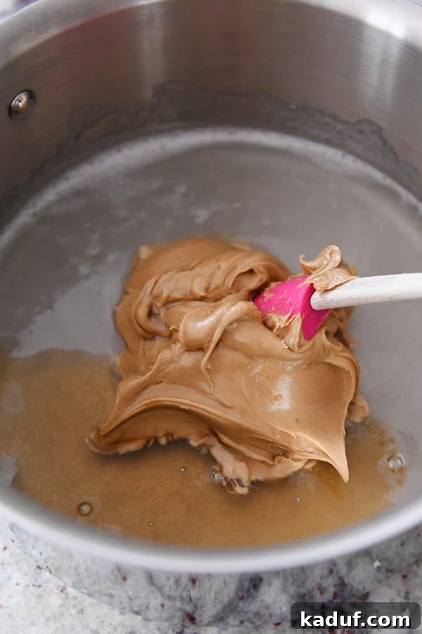 Gooey Peanut Butter Popcorn Bliss 7 Peanut butter and vanilla extract being stirred into the hot corn syrup and sugar mixture in a saucepan, beginning to form the caramel sauce.