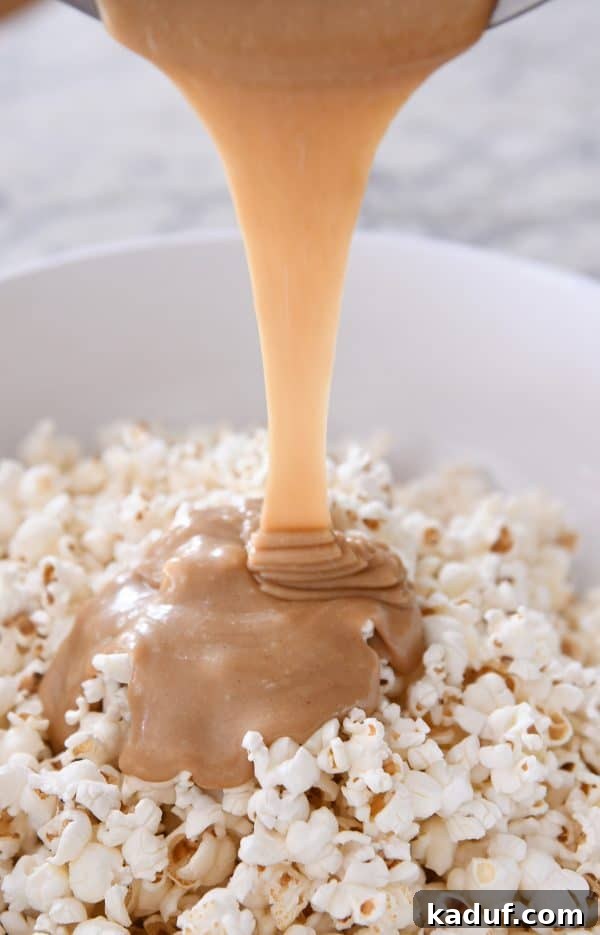 Gooey Peanut Butter Popcorn Bliss 9 Warm peanut butter caramel mixture being carefully poured over a large bowl of fluffy popcorn, initiating the coating process.