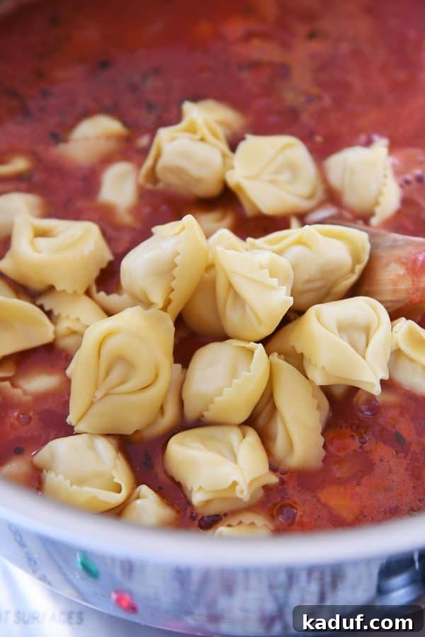 Fresh cheese tortellini being added to a simmering pot of rich Tuscan soup.