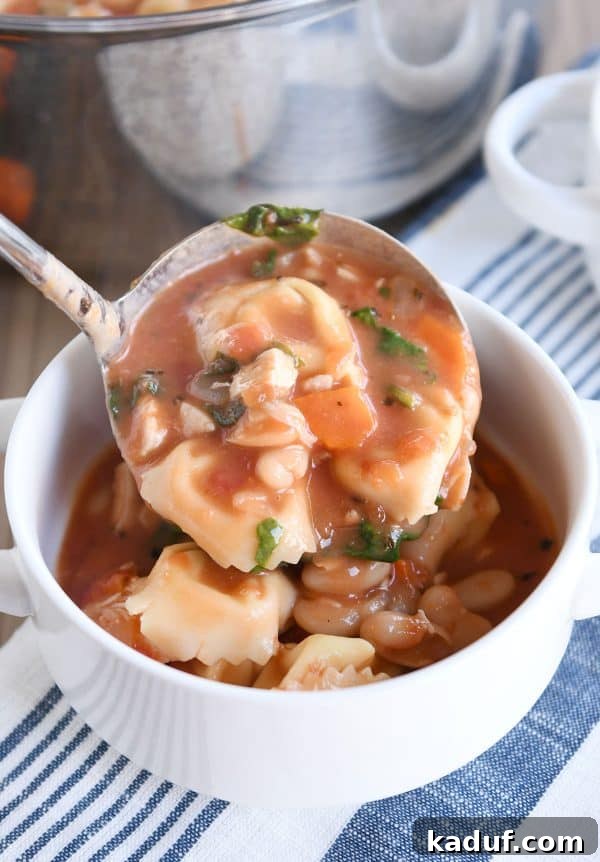 A ladle carefully pouring creamy Tuscan tortellini soup into a pristine white serving bowl.
