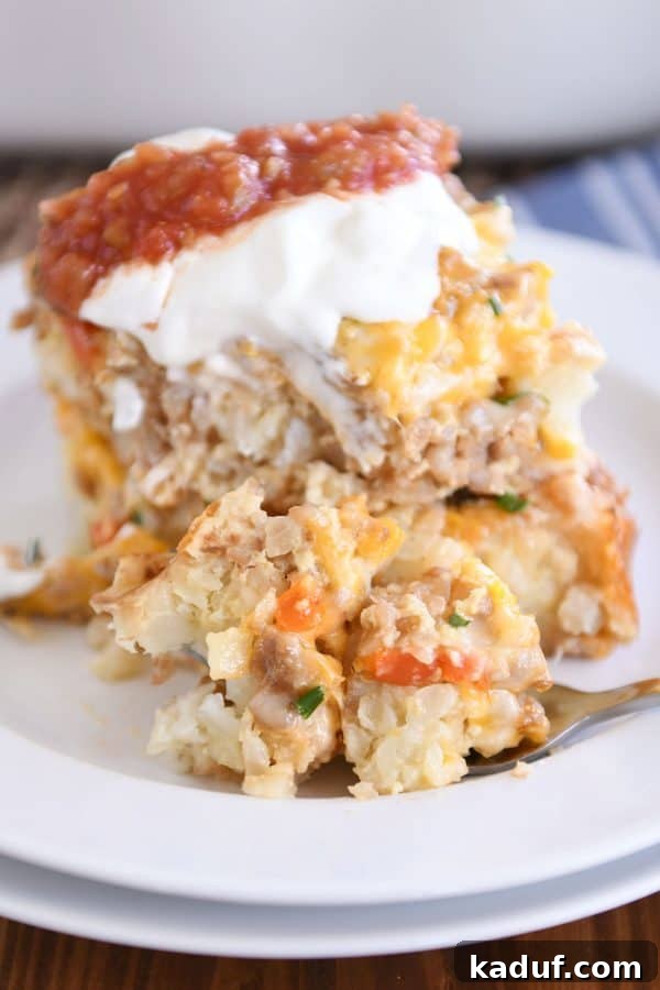 Dreamy Overnight Tater Tot Breakfast 11 Two squares of tater tot breakfast casserole stacked on each other on white plate with sour cream and salsa and fork taking a bite
