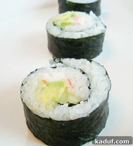 Homemade California Rolls Made Easy 2 Three perfectly formed California sushi rolls lined up on a pristine white plate, showcasing their vibrant green avocado, white rice, and nori.
