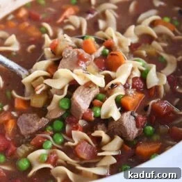 white slow cooker filled with beef vegetable noodle soup