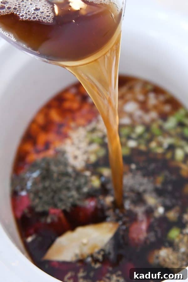 Hearty Slow Cooker Beef and Veggie Noodle Soup 5 Pouring beef broth into a slow cooker filled with beef and vegetables.