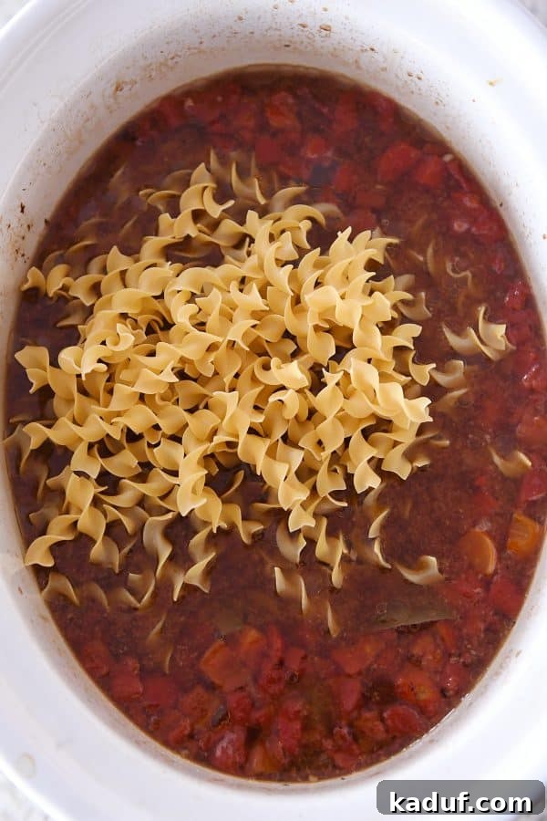 Hearty Slow Cooker Beef and Veggie Noodle Soup 7 Adding dry egg noodles directly to the hot beef noodle soup in the slow cooker.
