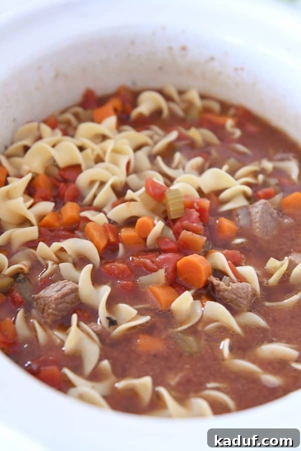 Hearty Slow Cooker Beef and Veggie Noodle Soup 8 White slow cooker brimming with a generous amount of finished beef vegetable noodle soup.