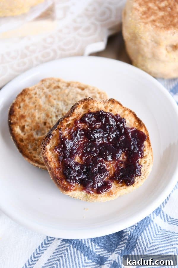 Split open easy homemade english muffin with butter and jam on white plate.