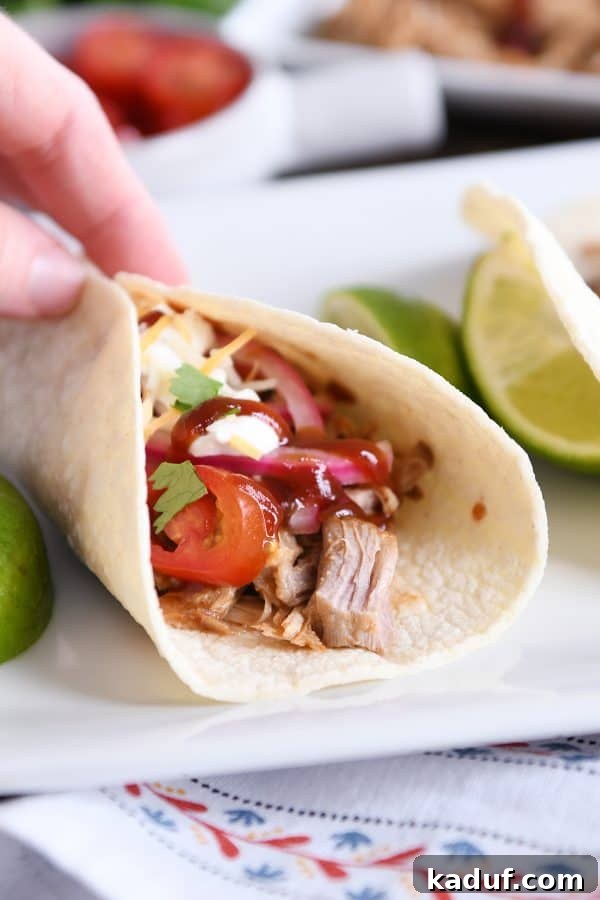 Tender BBQ Pork Tacos Instant Pot Slow Cooker Friendly 8 A hand holds a perfectly crafted Instant Pot BBQ pork taco, generously filled with tender pulled pork, pickled onions, and a drizzle of BBQ sauce, highlighting its delicious appeal.