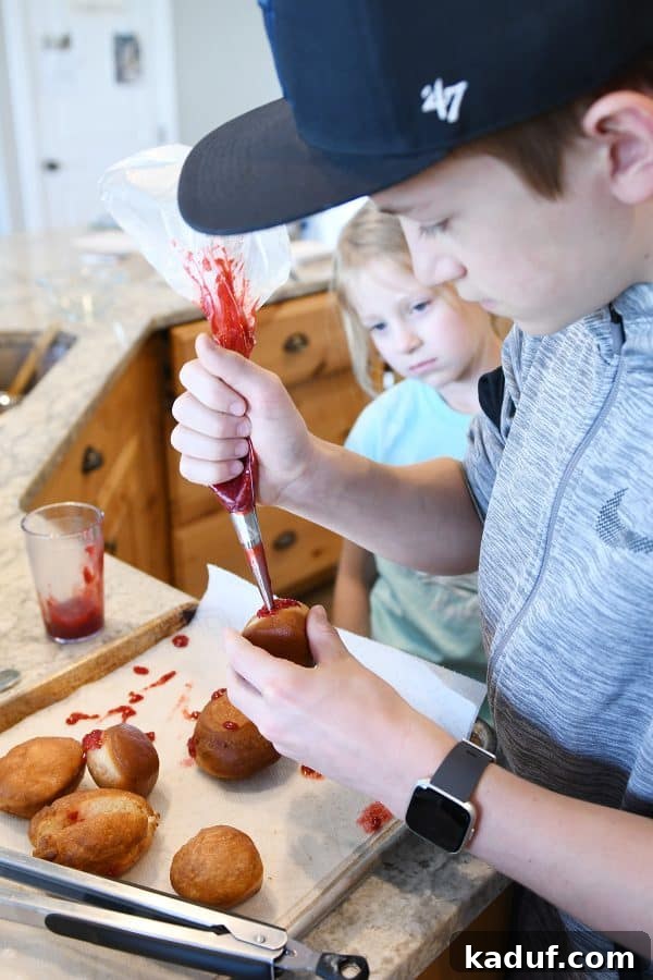 Melt-in-Your-Mouth Homemade Glazed Donuts 25 Piping vibrant raspberry jam into homemade donuts, ready for a sweet filling.