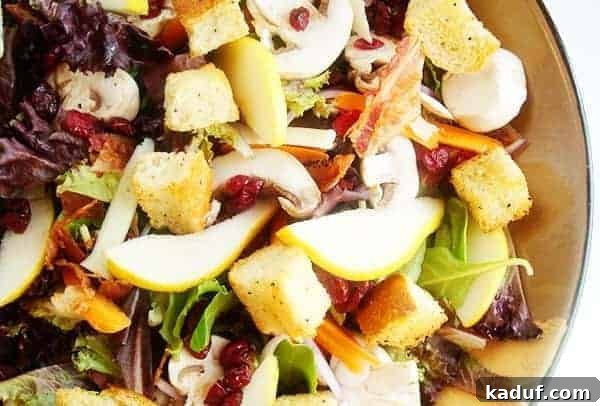 Fresh greens, thinly sliced pear, and golden croutons elegantly arranged in a large salad bowl, ready to be dressed.