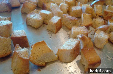 A batch of freshly baked, golden-brown bread cubes rests on a metal cookie sheet, perfectly toasted and ready to be served as homemade croutons.