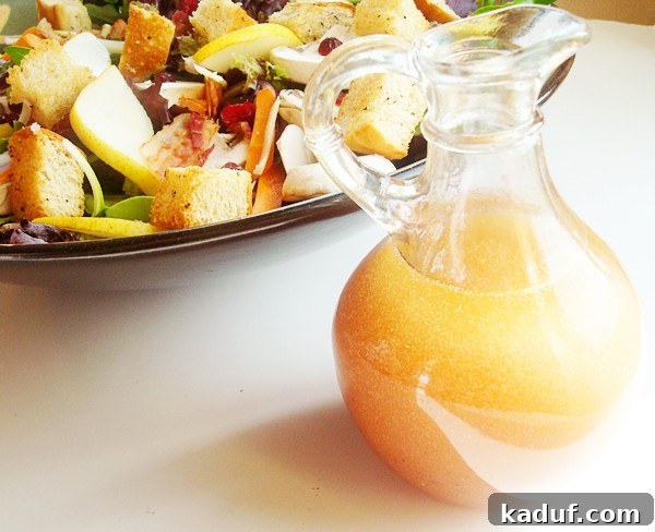 A small glass pitcher of rich red wine vinaigrette dressing sits beside a large bowl of gourmet green salad, ready to be drizzled.