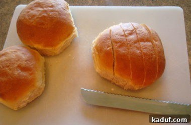 Homemade bread rolls are carefully sliced into even half-inch strips on a white cutting board, preparing them for the next step in making crispy croutons.