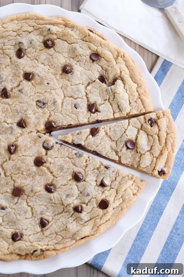 Effortless 12-Inch Monster Chocolate Chip Cookie 3 A generous slice of a giant chocolate chip cookie rests on a white platter, inviting indulgence with its golden edges and melty chocolate chips.