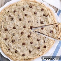Effortless 12-Inch Monster Chocolate Chip Cookie 5 A delicious giant chocolate chip cookie on a white platter, with a slice removed, revealing its soft and chewy interior.