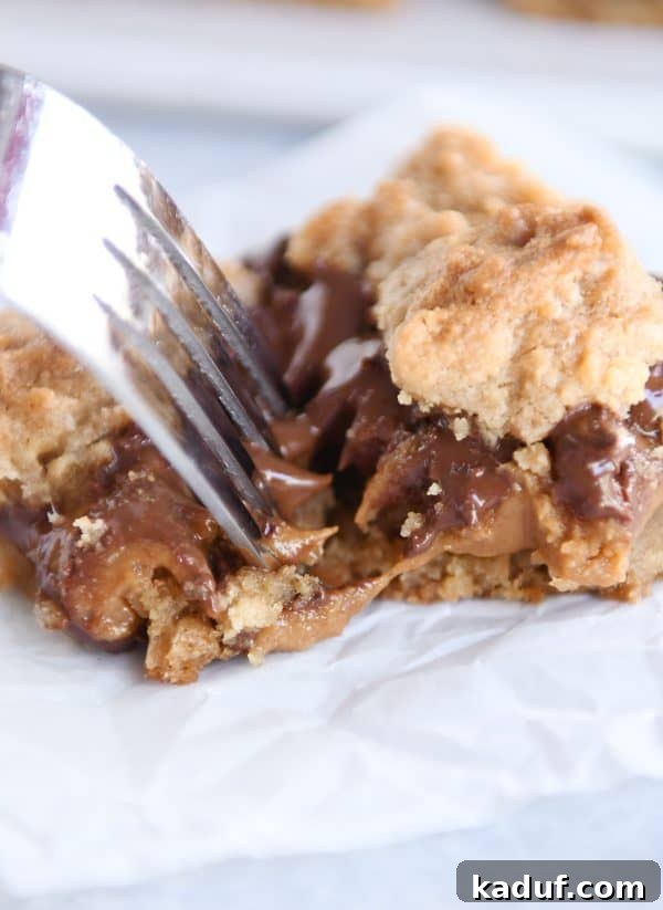 A fork lifts a warm, gooey bite of caramel cookie bar from the pan, highlighting its soft texture.