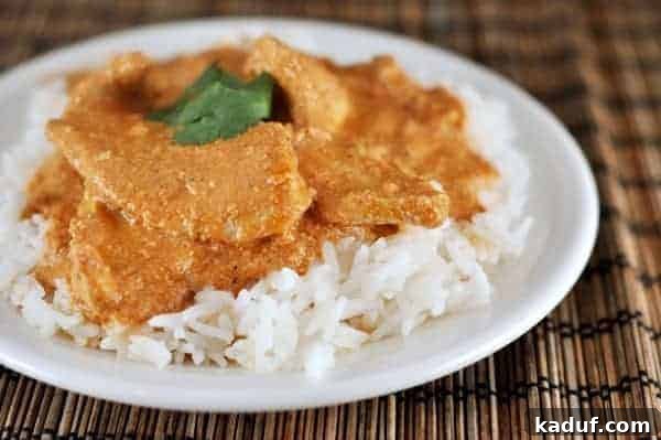 India's Beloved Creamy Chicken 2 A serving of white rice topped with generous portions of rich orange chicken tikka masala on a clean white plate.