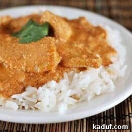Close-up of a bowl of Chicken Tikka Masala with a side of white rice, garnished with fresh cilantro.
