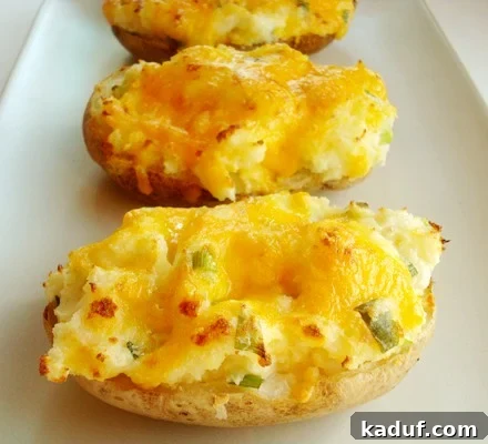 Loaded Double-Baked Potatoes 3 Baked potatoes cut in half with melted cheese and chopped chives on a white plate.