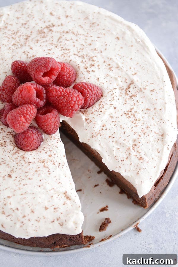Cloud Nine Chocolate Mousse Torte 3 Top-down view of a round double chocolate mousse torte, generously covered with whipped cream and fresh raspberries, with one slice removed.