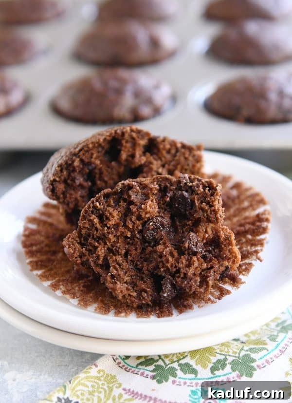 Wholesome Double Chocolate Zucchini Muffins 2 A perfectly baked, moist double chocolate zucchini muffin, halved to reveal its rich, chocolatey interior and flecks of zucchini, sitting on a muffin liner.