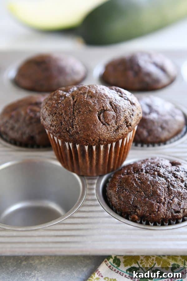 Wholesome Double Chocolate Zucchini Muffins 3 Freshly baked double chocolate zucchini muffin resting on top of a muffin tin, showcasing its appealing dome and rich brown color.