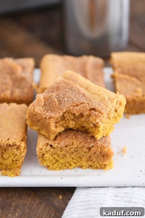 Harvest Spice Pumpkin Snickerdoodle Bars 5 Two pumpkin snickerdoodle bars stacked on white tray with bite taken out of top bar, highlighting their perfect texture.