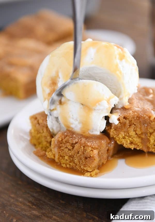 Harvest Spice Pumpkin Snickerdoodle Bars 6 Fork taking bite out of easy pumpkin snickerdoodle bar with vanilla ice cream and butterscotch sauce on white plate. A luxurious fall dessert experience.