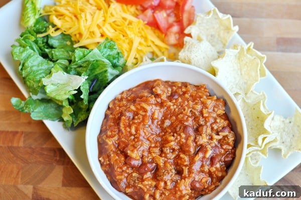 Crunchy Taco Salad Dip 3 Top-down view of a white bowl filled with a rich taco meat and rice mixture, elegantly arranged with fresh accompaniments such as crisp shredded lettuce, grated cheddar cheese, juicy diced tomatoes, and a generous border of crunchy tortilla chips, ready for a delightful dipping experience.