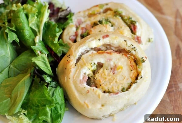 Savory Swirl Delights 2 Two golden-brown savory spiral stuffed rolls, generously filled with ham, broccoli, and melted cheese, beautifully arranged next to a fresh bed of green lettuce on a pristine white plate.