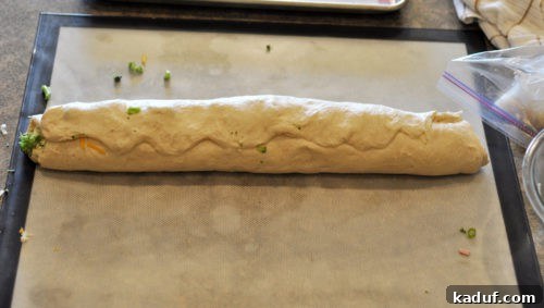 Savory Swirl Delights 5 The completed log of bread dough, filled with savory ingredients, with its seam firmly pinched and sealed, ready for slicing.