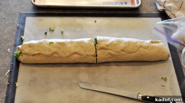 Savory Swirl Delights 6 The tightly rolled log of savory bread dough, now sliced in half, revealing a beautifully intricate spiral pattern of ham, broccoli, and cheese within its cross-section.