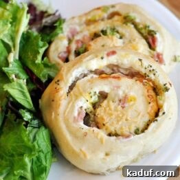 A close-up view of a baked savory spiral roll, highlighting its golden crust and the visible swirls of creamy ham, broccoli, and cheese filling.