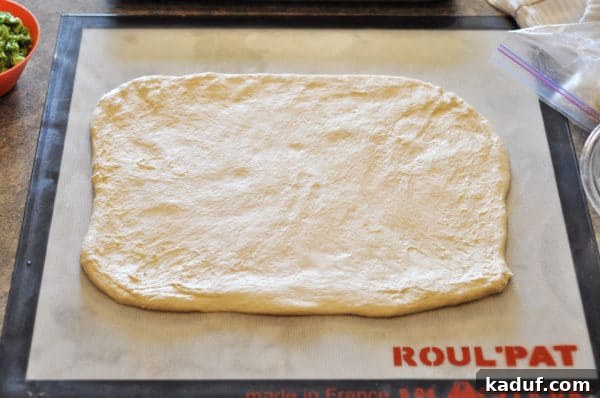 Dough Rolled Out Homemade bread dough meticulously rolled out into a large, rectangular shape on a light-colored silicone baking mat, ready for the next layer of ingredients. The dough is smooth and evenly spread.