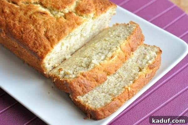 Luscious Buttermilk Banana Bread 11 Loaf of golden-brown banana bread with two perfectly cut slices on a white serving plate, highlighting its tender interior.