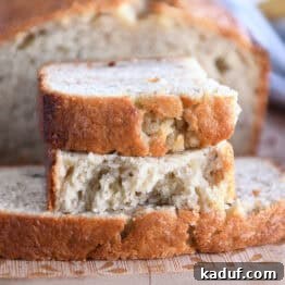 Two half slices of banana bread on wood cutting board, showcasing its tender crumb.