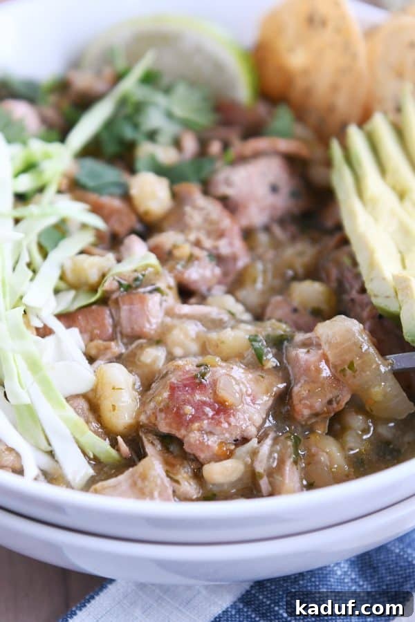 Easy Slow Cooker Posole 3 Seasoned pork, hominy, broth, cabbage, avocado in white bowl.