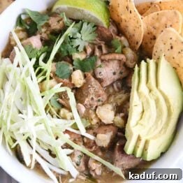 Easy Slow Cooker Posole 9 top down view of slow cooker posole in white bowl with shredded cabbage, sliced avocado, tortilla chips and lime wedge