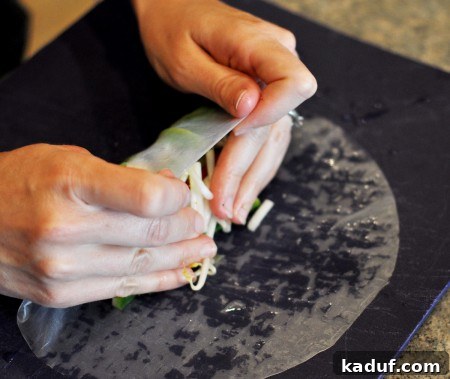 Rolling2 Hands gently rolling up a rice wrap with fresh vegetables inside.