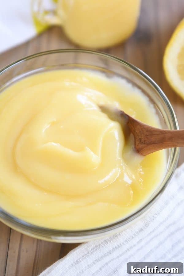 Easy Instant Pot Lemon Curd 3 A clear glass bowl filled with creamy Instant Pot lemon curd, with a wooden spoon resting inside, highlighting its smooth consistency.