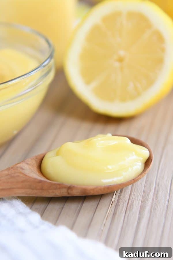 Easy Instant Pot Lemon Curd 4 A wooden spoon holding a generous scoop of glistening lemon curd, placed on a rustic wooden board.