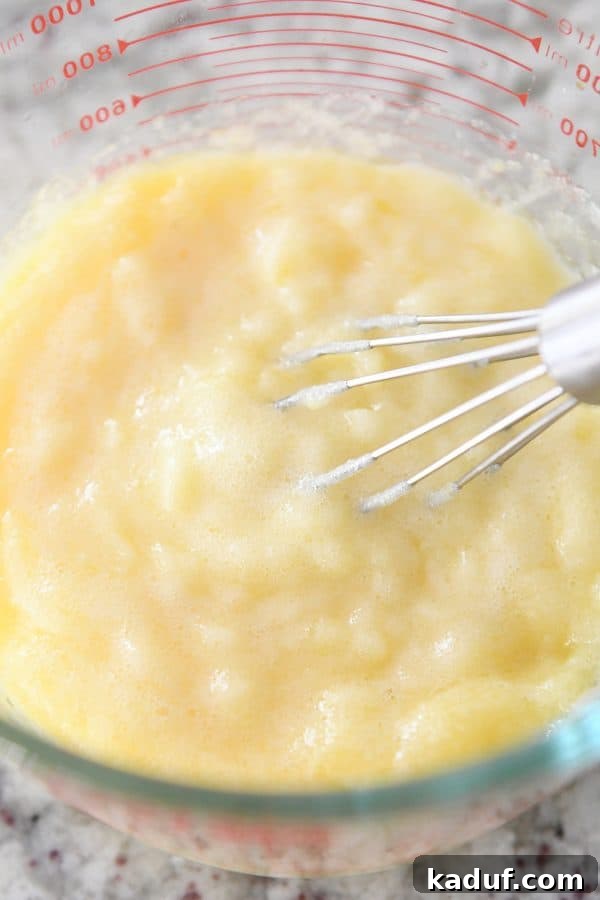 Easy Instant Pot Lemon Curd 6 A whisk vigorously mixing lumpy, freshly cooked Instant Pot lemon curd in a glass bowl, before it reaches its smooth consistency.