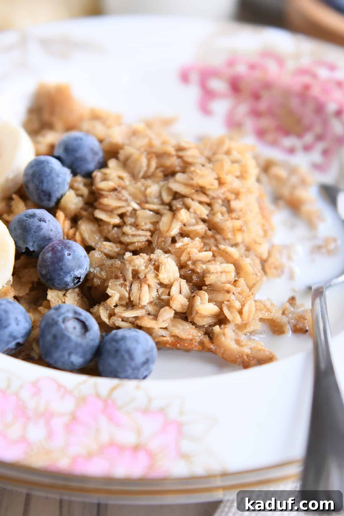 Effortless Amish Overnight Baked Oats 2 A bowl of baked oatmeal in a floral dish, garnished with blueberries and sliced bananas, accompanied by a spoon and a glass of milk. This delicious, hearty breakfast is perfect for busy mornings.