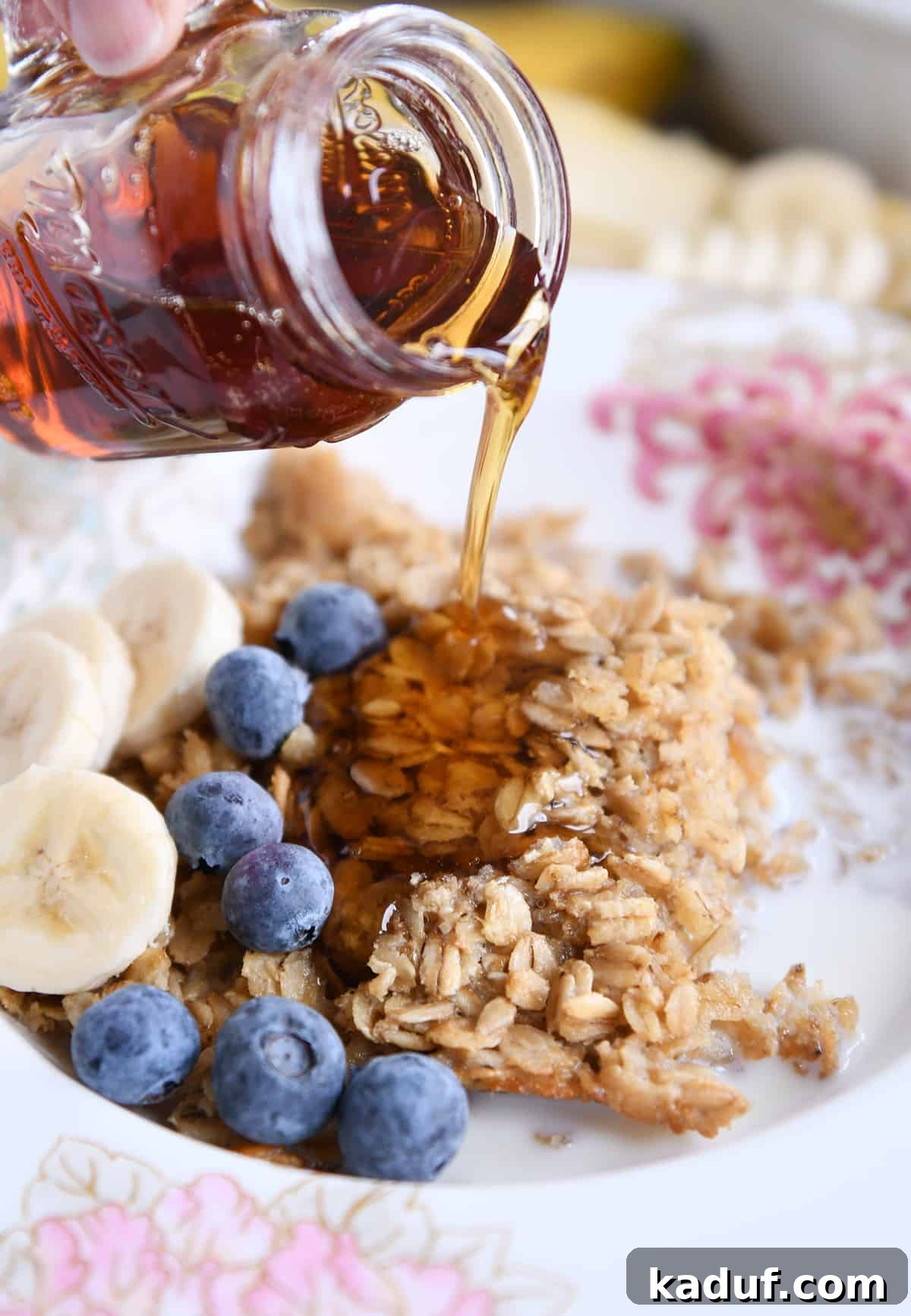 Effortless Amish Overnight Baked Oats 3 Maple syrup being drizzled over a warm bowl of Amish baked oatmeal, topped with fresh blueberries and sliced bananas, highlighting its delicious serving suggestion.