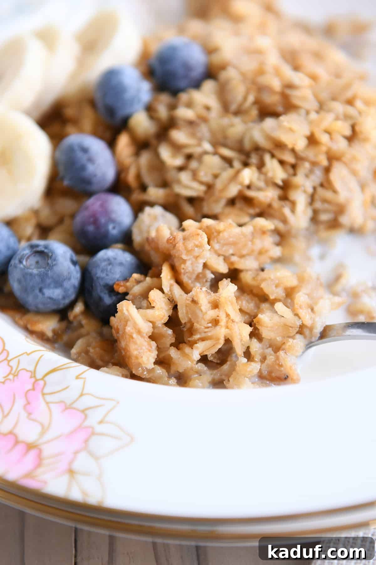 Effortless Amish Overnight Baked Oats 8 A spoon lifts a perfect spoonful of warm Amish baked oatmeal, garnished with fresh blueberries and sliced bananas, from a beautiful floral bowl, inviting a taste.