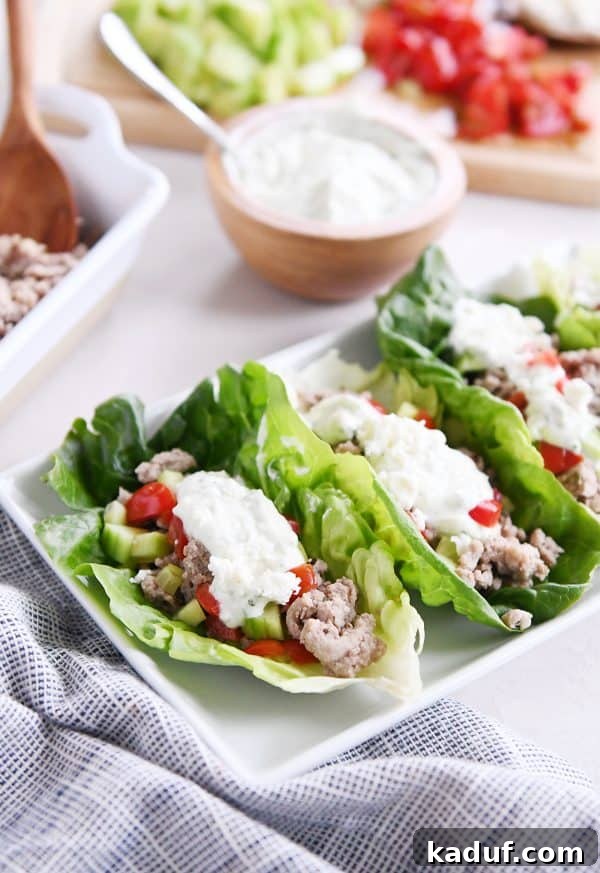 Zesty Greek Lettuce Boats 6 Three perfectly formed Greek lettuce wraps on a white serving tray, garnished with fresh cucumbers, tomatoes, and a generous drizzle of feta mint dressing.