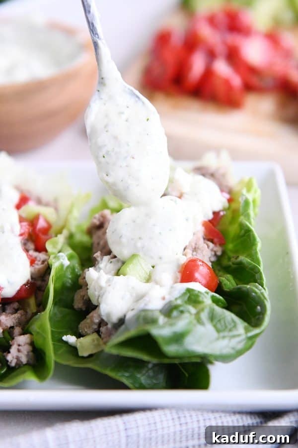 Zesty Greek Lettuce Boats 7 Close-up of creamy feta dressing being drizzled generously over Greek lettuce wraps arranged on a pristine white tray.