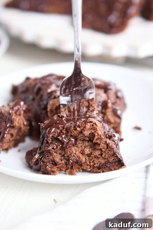 Divine Triple Chocolate Scones 3 A fork delicately scooping a piece from a chocolate scone adorned with glaze on a pristine white plate, showcasing its tender interior.