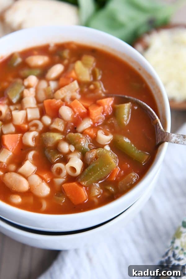 Rustic Italian Minestrone 7 A spoon resting in a bowl of classic minestrone soup, served in a stack of white bowls.